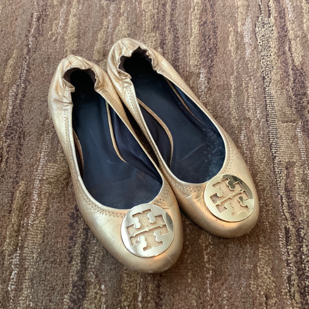 Tory Burch gold metallic flats with gold pendant.